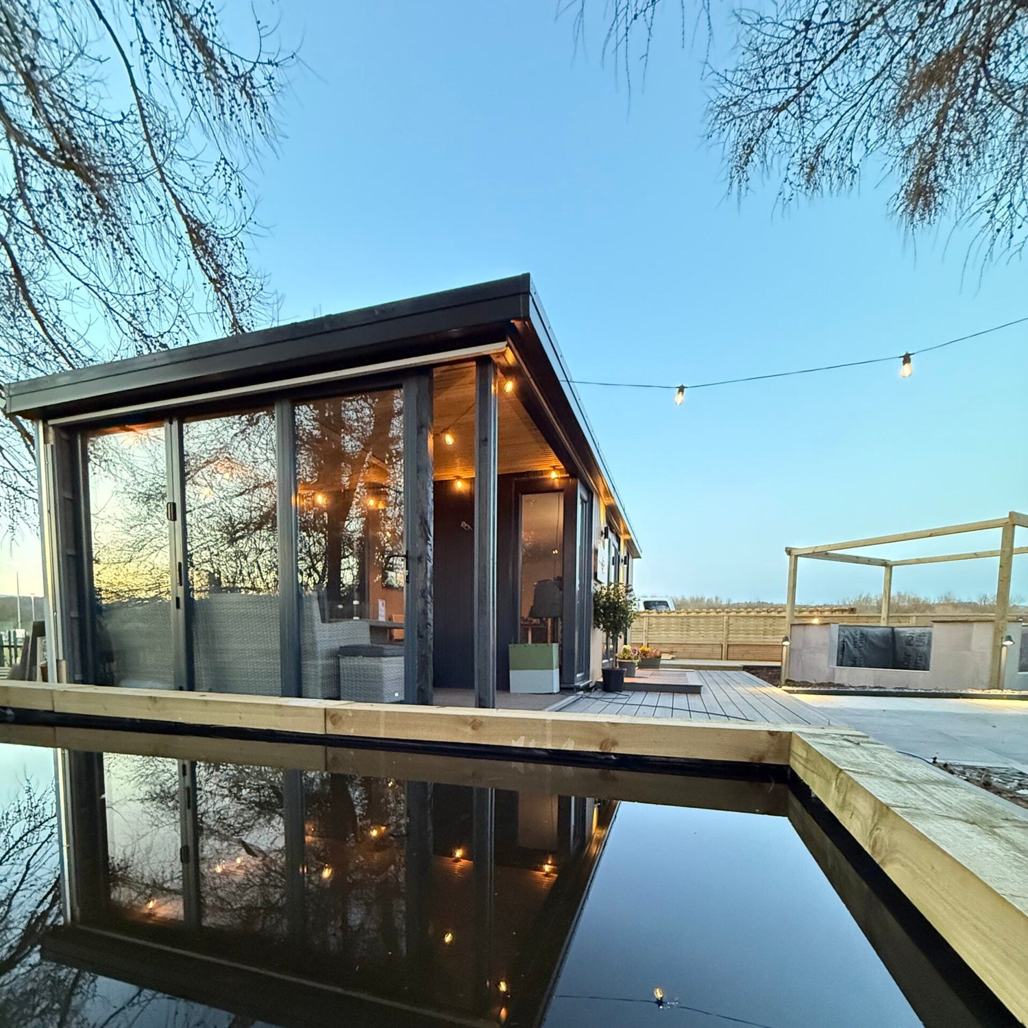 Modern garden room by a body of water with trees in the background