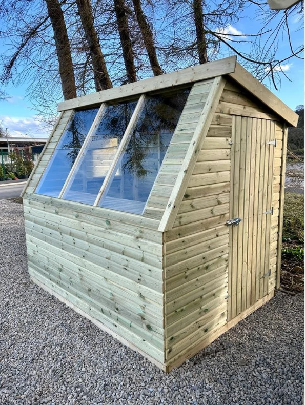 Wooden Potting Shed with glass panels on a gravel surface with trees in the background